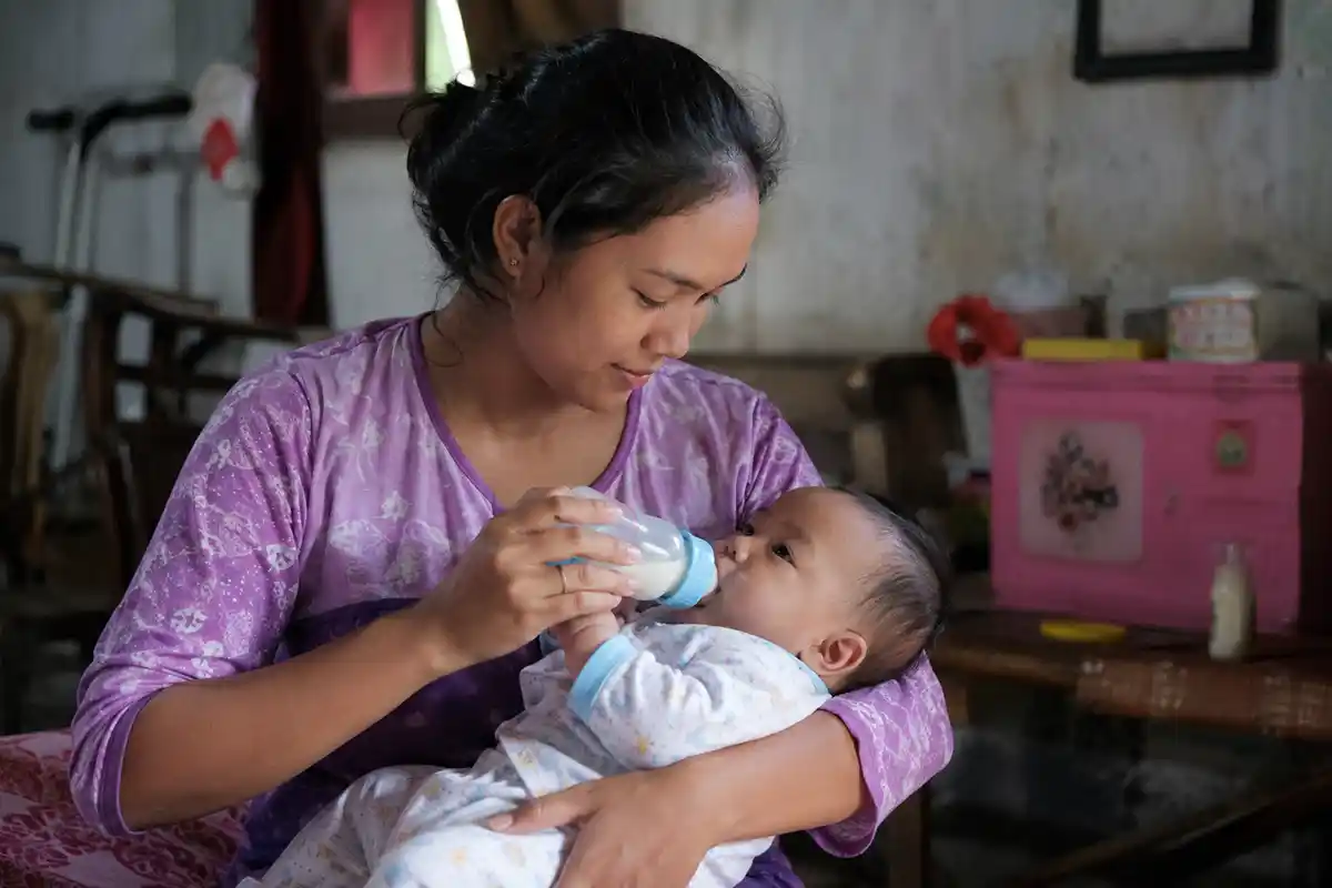 Seorang ibu sedang memberikan susu kepada bayinya di rumah.