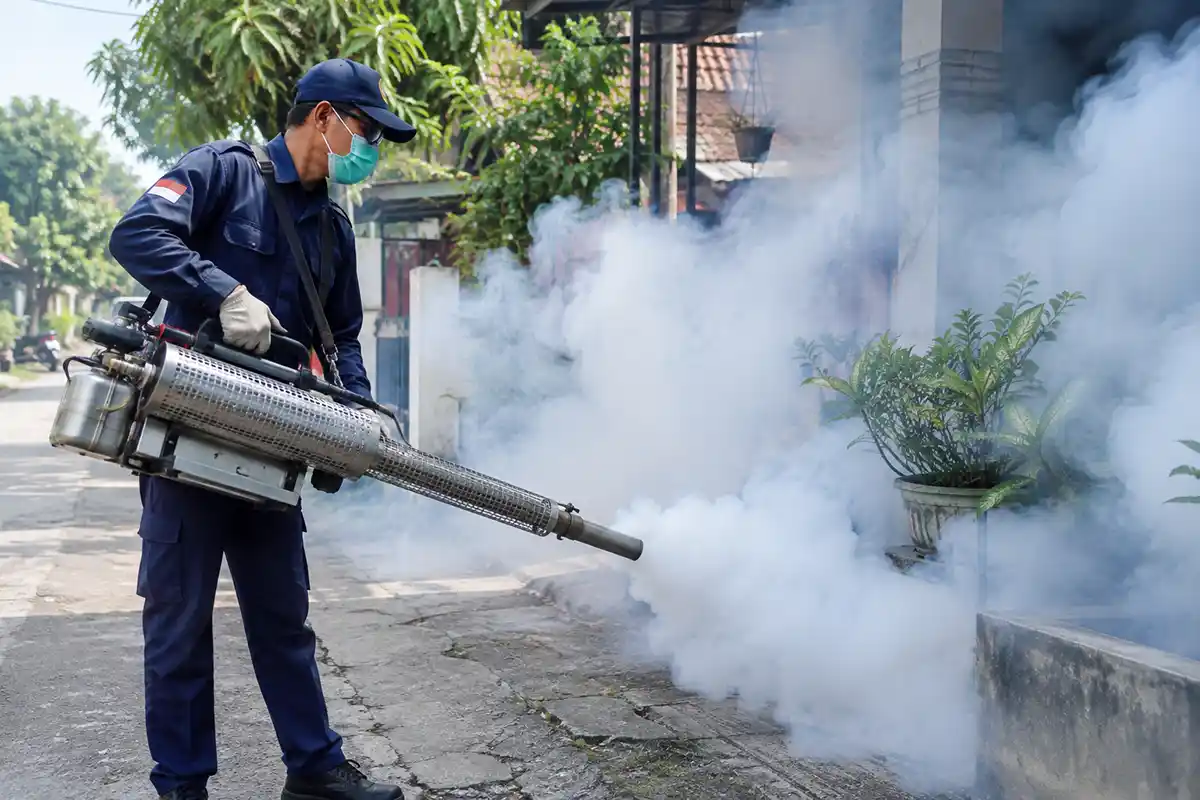 Petugas mengenakan masker dan seragam menyemprotkan asap fogging di area permukiman untuk membasmi nyamuk DBD.