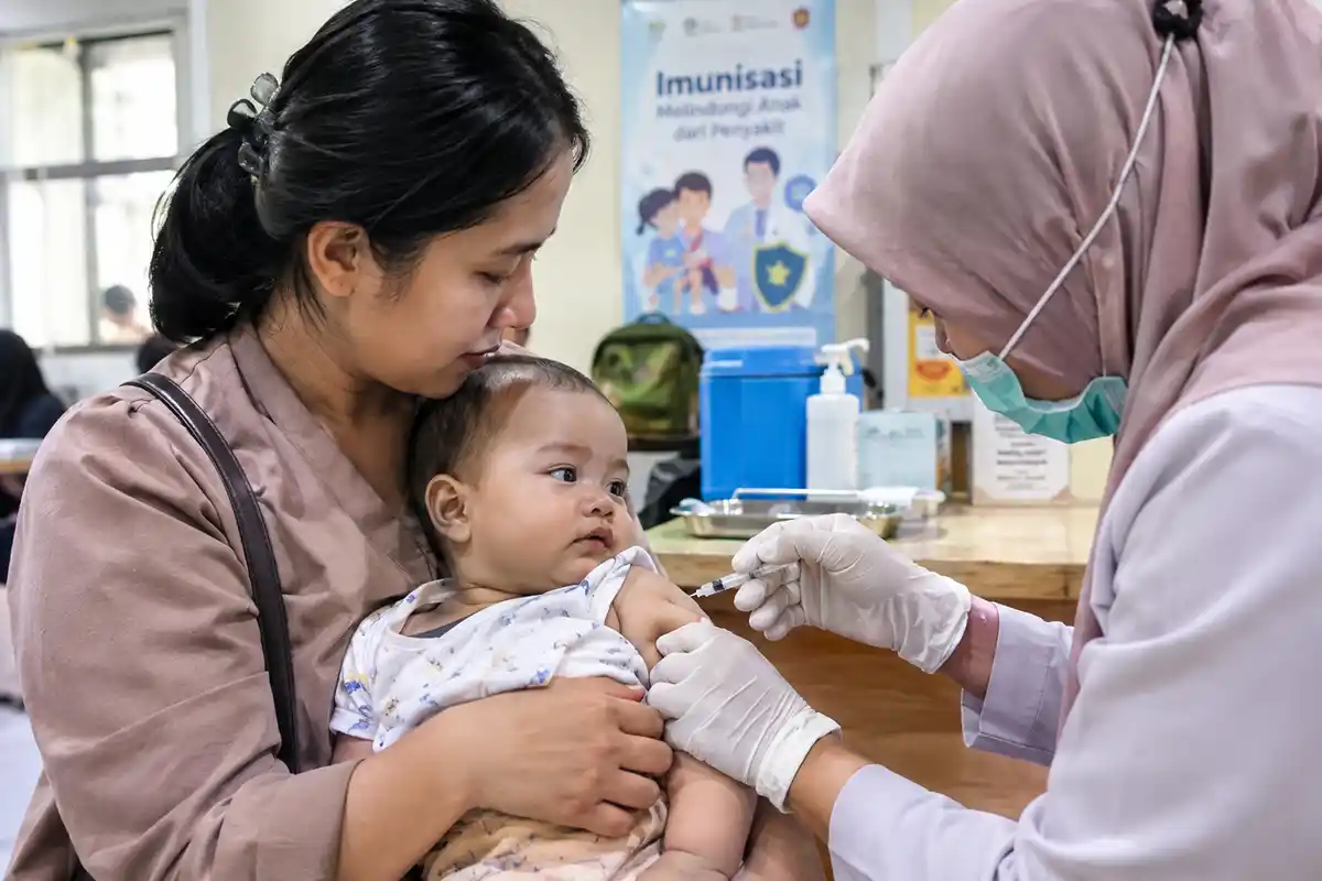 Seorang bayi tenang dipangku ibunya saat menerima suntikan vaksin imunisasi dari tenaga kesehatan.