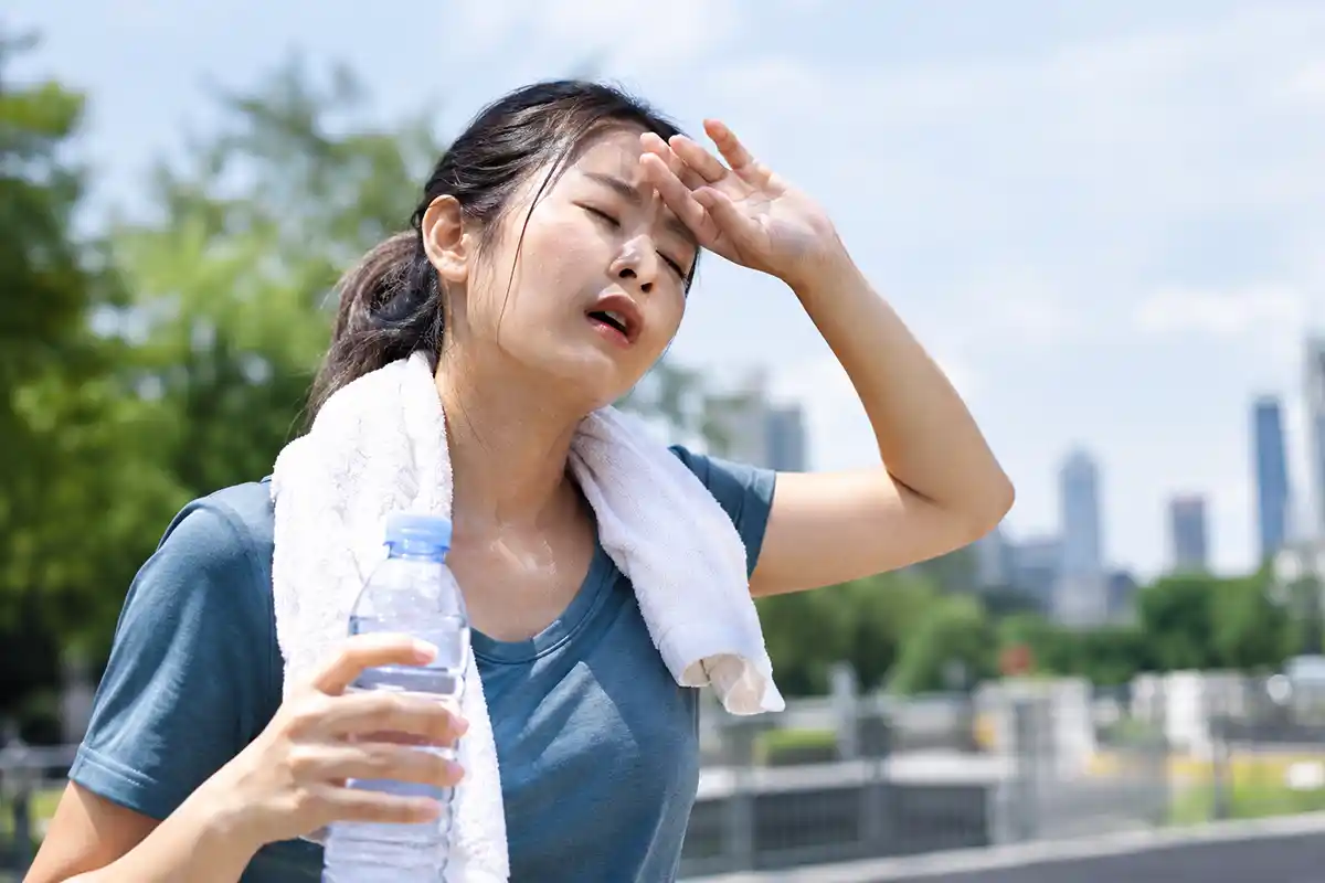 Seorang wanita menyapu keringat di dahi sambil memegang botol air minum di luar ruangan saat cuaca terik.